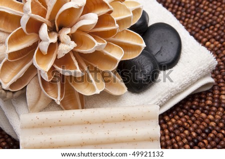 Spa scene with paper lotus flower, massage stones, towel and textured soap.