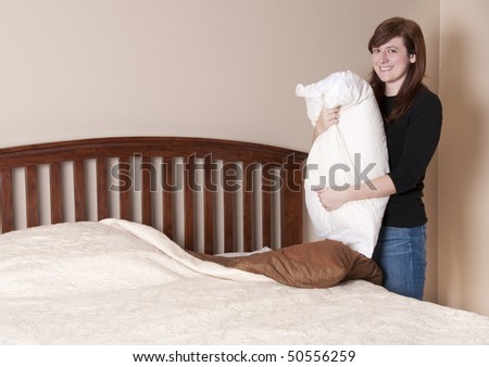 Brunette woman makes the bed in a neutral colored bedroom.