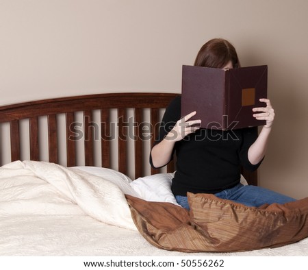 Brunette Woman Reads in Bed in a Neutral Colored Bedroom.