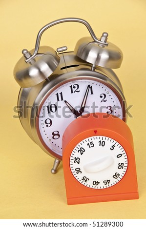 Silver Alarm Clock and Bright Orange Timer on Yellow Background.