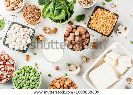 Healthy diet vegan food, veggie protein sources: Tofu, vegan milk, beans, lentils, nuts, soy milk, spinach and seeds. Top view on white table.