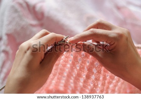 closeup of female hands knitting pink sweater