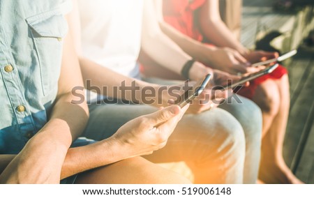 Summer sunny day, close-up of smartphones in the hands of women sitting outdoors on wooden steps. Meeting friends. Girls using digital gadgets.
