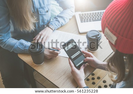 Top view, close-up smartphone in female hands. Meeting of two friends in cafe.Girls learn online, drinking coffee. First woman takes notes,and second uses a smartphone.Freelancers work outside office.