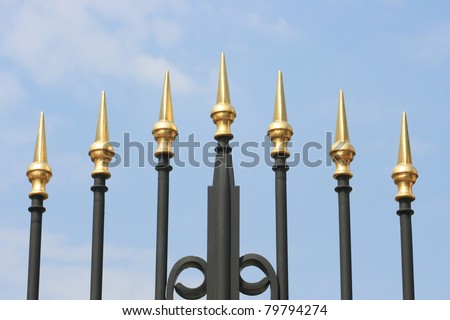 Wrought iron spikes of a gate, with a blue sky background