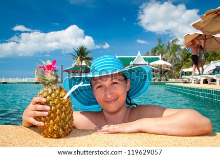 Beautiful woman in hat enjoying pineapple drink at swimming pool of Thailand
