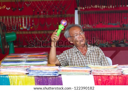 KHAO LAK, THAILAND - NOV 05: Unidentified old man selling clothes on the local market in Khao Lak. This market is also tourist attraction in Phang Nga province, Thailand on Nov.05, 2012.