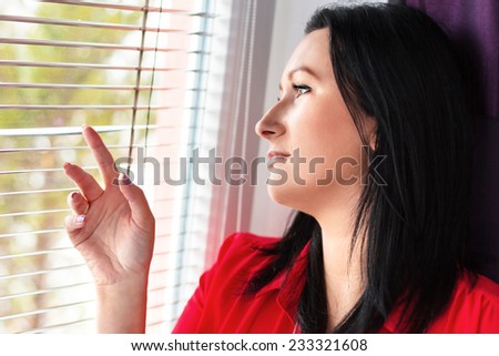 Expectation. Woman looks out of the window through a jalousie
