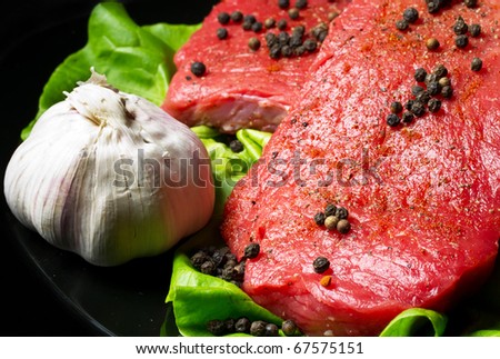 Raw beef steak with garlic and black pepper on black plate