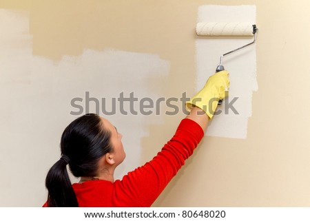 Young adult woman painting interior wall of house