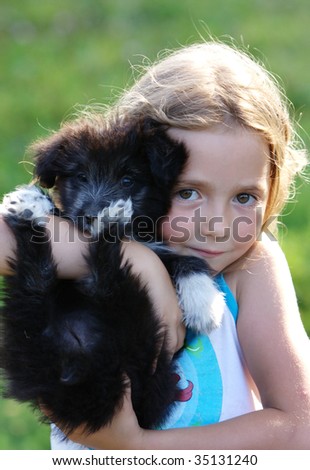 Smiling little girl hugging a big black dog in an outdoor setting