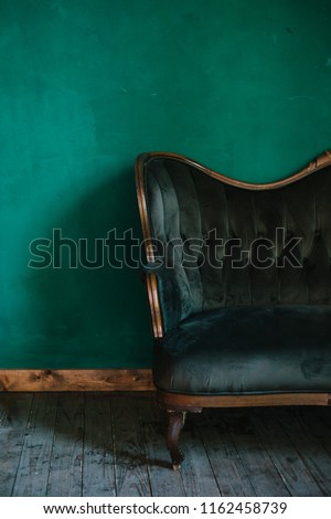 classic interior in dark green colors. vintage velvet sofa near emerald wall. Armrest of luxurious green sofa, close-up. Luxury vintage green couch in the room. Antique wood sofa couch.