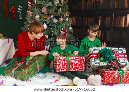 Mother with her happy kids have got gift boxes under Christmas tree