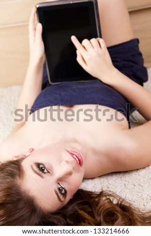 The girl lying on her back, and pointing on a tablet PC with one finger.