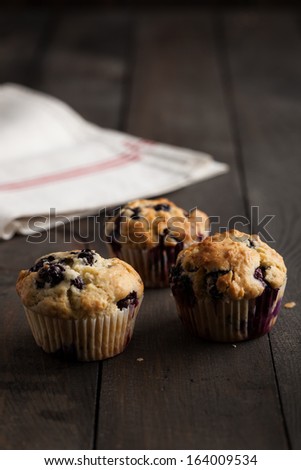 Freshly baked blueberry muffins served with vintage french linen on dark wooden table. Moody lighting, rustic and natural atmosphere.