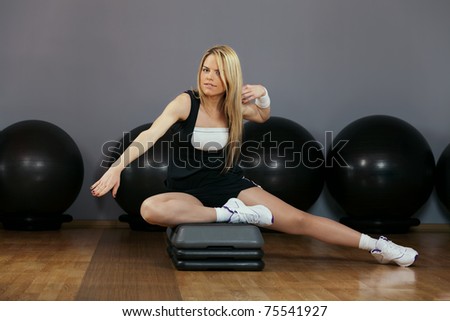 Beautiful blond young woman performing step aerobics exercise in a gym