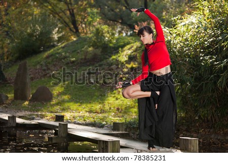 Outdoor portrait of a beautiful young woman with long, black hair, in a tree yoga pose in nature. Taken in late fall, with shallow depth of field.