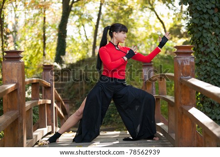 Attractive woman dressed in manga style practicing martial arts on a wooden bridge in the woods. Shallow depth of field.