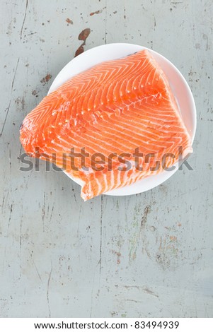 Big, raw, fresh and juicy salmon steak in a white plate on a rustic dinner table.