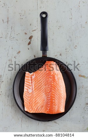 Big fresh salmon steak in black frying pan on rustic diner table, taken directly from above.