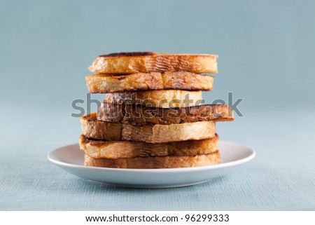 Close-up of a stack of French toast on a white plate served on a table with light blue tablecloth.
