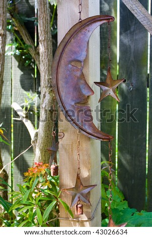 Rusty metal half moon and stars garden ornament hanging from wooden post.