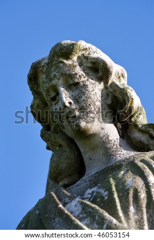 Weathered stone Graveyard Monument of an angel against vivid blue sky.