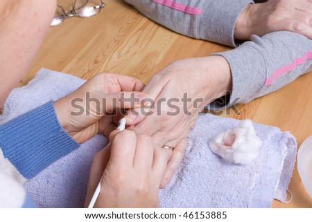 Older senior woman with arthritic hands receiving home spa treatment / manicure.