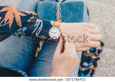 street style fashion details. close up, young fashion blogger wearing a floral jacker, and a white and golden analog wrist watch. checking the time, holding a beautiful suede leather purse.