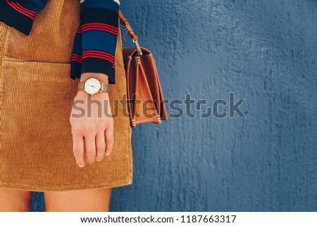 close up, young fashion blogger wearing a corduroy dress and a white and golden analog wrist watch. checking the time, holding a beautiful  leather purse. street style fashion details.