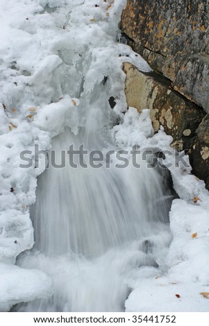 water bursting through snow pack down waterfall in winter