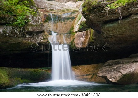 milky waterfall falling into a pool with rocks and greenery surrounding