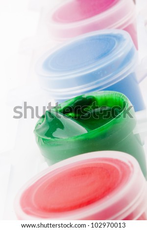 Open plastic container with green paint next to containers with other colors on a white background.