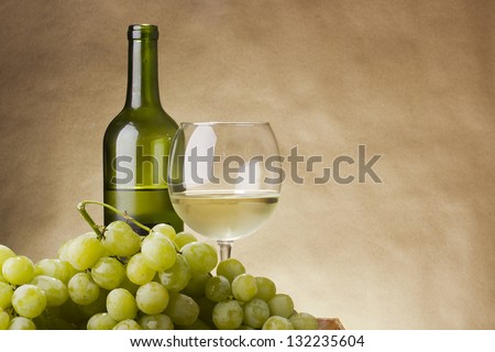 Bottle and glass of white wine and a bunch of grapes.