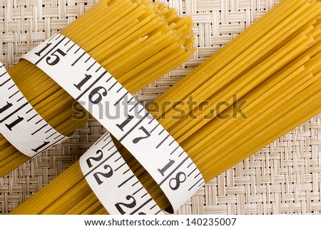 Directly above photograph of golden pasta tied with measuring tape.