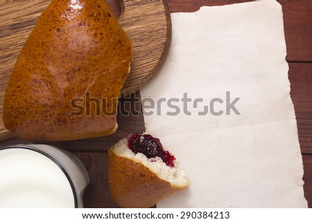 Roll with jam on a kitchen cutting board, a glass of milk and paper for informational message.