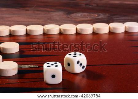 Board game a backgammon. In the foreground cubes with figures for game, on a background white counters.