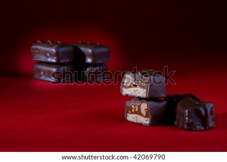 The chocolate with nuts is cut half-and-half. A red background, on a back background some chocolates.