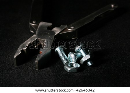 Bolts and nuts with flat-nose pliers on a black fabric.