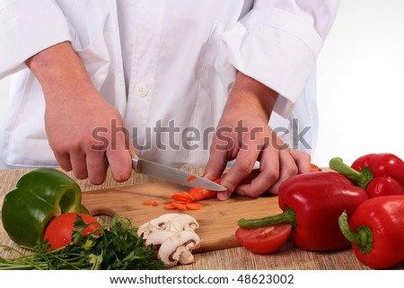 The cook cuts carrots on a chopping board with other vegetables.