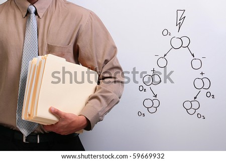 Man in a shirt and a tie holding manila folders while standing next to a drawing of ozone formation.