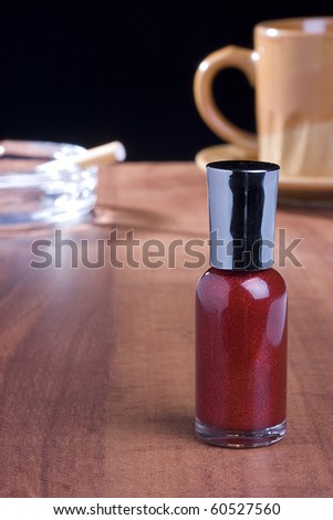 Red nail polish standing on a coffee table in front of a cup of coffee and an ashtray.