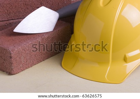 Yellow hard hat next to bricks and a stonemason\'s tool.