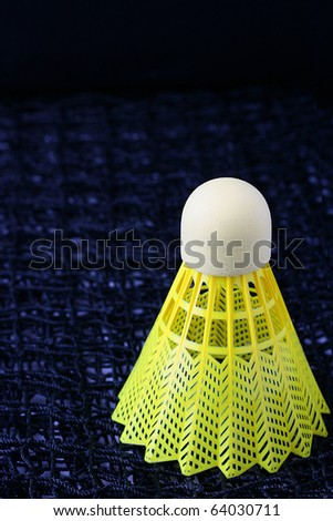 Bright yellow badminton shuttlecock sitting on a badminton net.