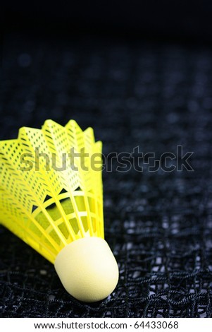 A bright yellow badminton shuttlecock laying on a badminton net.
