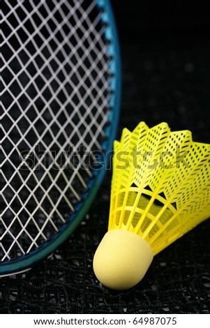 Bright yellow badminton birdie and a badminton racquet laying on a net.