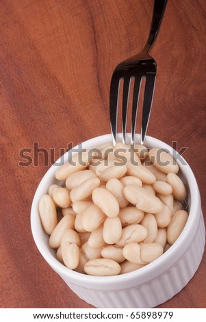 White canned beans in a white ceramic bowl with a fork.