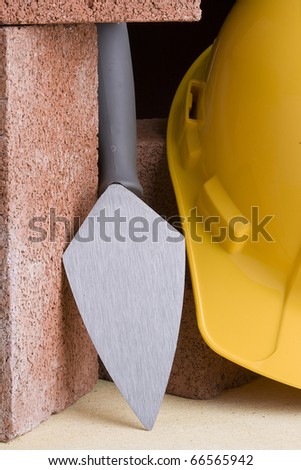 Stonemason\'s trowel next to red bricks and a yellow hard hat.