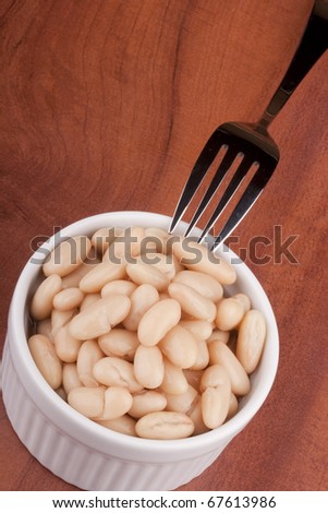 White canned beans in a white ceramic bowl with a fork.