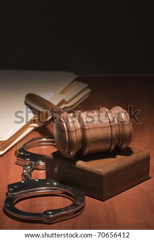 Handcuffs and a wooden gavel in front of manila folders.